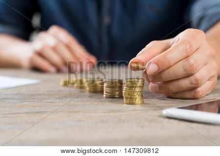 Man putting money coins on rising lines. Close up of hand of businessman stacking euro coins on wooden table. Male hand putting money coin stack for growing business.