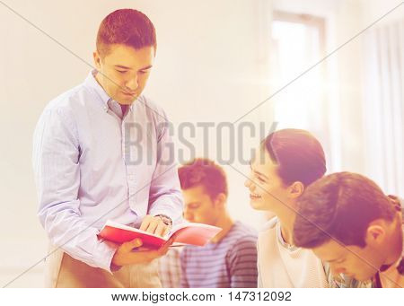 education, high school, teamwork and people concept - group of smiling students and teacher with notebook in classroom