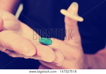 closeup of a young man with a blue pill in one hand and a condom in the other hand, with a filter effect