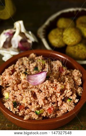 closeup of an earthenware casserole whit couscous with vegetables and some falafel in a plate in the background, on a wooden table
