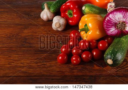 Heap of fresh organic tasty vegetables on brown wood with copy space for menu or recipe. Healthy natural food on wooden table background. Bright peppers and other cooking ingredients top view