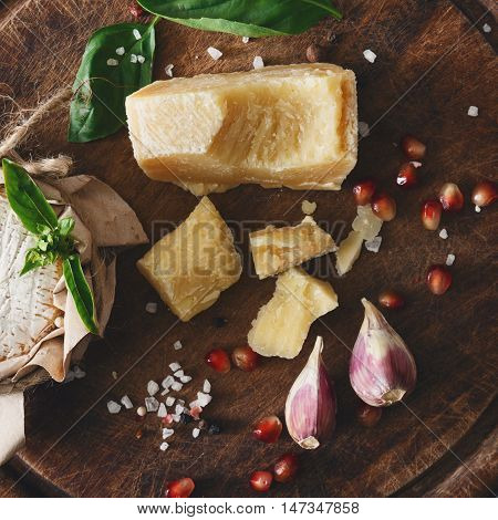 Cheese delikatessen closeup on rustic wood. Wooden desk with parmesan, camembert and brie cuts decorated with garlic, pomegranate and rosemary, top view image