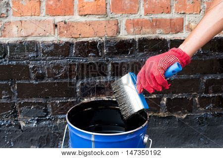 Roofer covered brick wall bitumen primer for improving adhesion during surfacing contiguity with rolled waterproofing during the installation of flat roof.