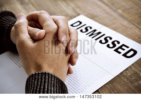 closeup of the clasped hands of a young caucasian man on a document with the text dismissed, placed on a rustic wooden table