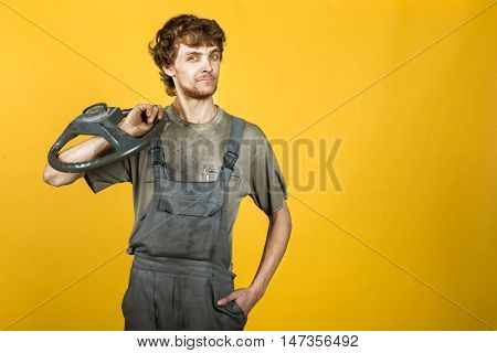 Handsome smiling mechanic posing in work clothes, he leans on the car's door on the background of yellow bright wall