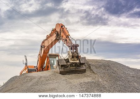 Excavator on top of a ballast pile - Frontal view of an orange excavator climbed on top of a ballast pile.