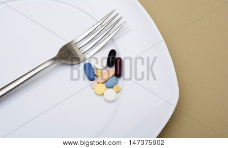 Colorful capsules and pills on plate with fork knife - healthy diet.