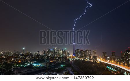 Powerful Lightning bolt strikes over Toronto City in a strong, hot, and humid thunderstorm.  Stormy night in August, Toronto skyline with weaker flashes of lightning behind the city.