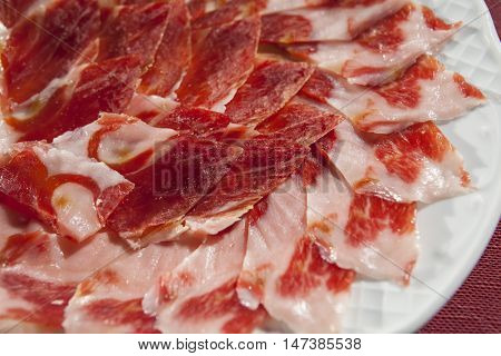 Circular decorative arrangement of iberian cured ham on plate. Selective focus point