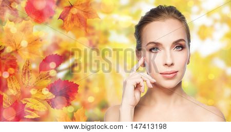 beauty, people and skin care concept - beautiful young woman showing her cheekbone over natural autumn leaves and lights background