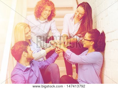 business, office, gesture and startup concept - smiling creative team with hands on top of each other sitting on staircase