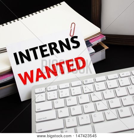 Word text Interns wanted on white paper card on office table / business concept