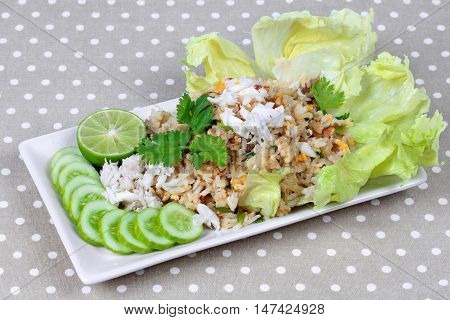 Fried rice with crab topped streamed crab,halve green lemon,sliced cucumber,lettuce and coriander  on gray. Side view.