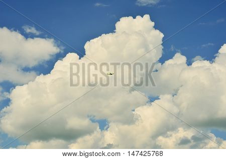 The plane flies in the white clouds and blue sky