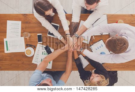 Team put hands together, show connection and alliance, top view of working table. Teambuilding in office, young businessmen and women in casual unite hands for teamwork and cooperation at new project.