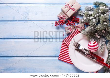 Christmas table setting. White plate knife and fork napkin and christmas decorations in white and red colors on blue wooden table. Top view. Selective focus. Place for text.