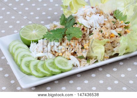 Close up of fried rice with crab topped streamed crab,halve green lemon,sliced cucumber,lettuce and coriander on gray. Selective focus.