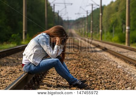 The girl in denim suit sits on rails desperately bent head supports her hands.