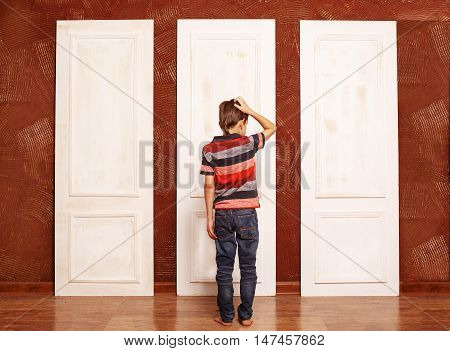 concept of choice. doubting boy stands in front of three closed doors. view from the back