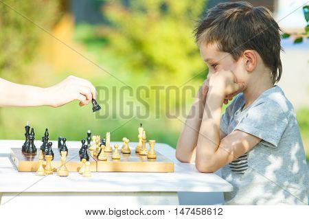 boy pondering chess game. kid playing chess with an adult outdoors. the concept of education