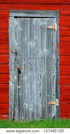 Closeup of smokehouse door. Building is painted red is wooden and has cracked boards and worn paint.