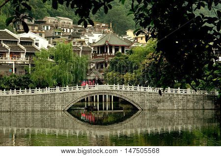 Yangshuo China - April 30 2008: Single arch bridge reflected in the tranquil waters of a lagoon in the city's old quarter with traditional Chinese buildings