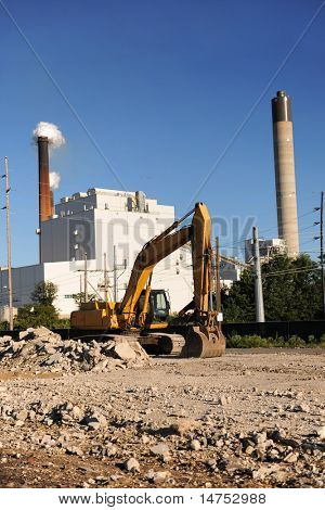 Sito industriale con bulldozer in primo piano e di fabbrica con ciminiere in background