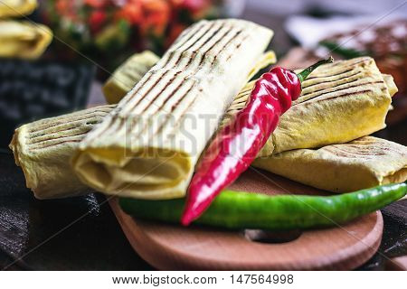 Breakfast two spicy delicious burritos mexican fast food dinner on wooden board wood table decorated with red and green hot peppers. Eggs pepper potatoes vegetables meat inside. Healthy lunch snack.
