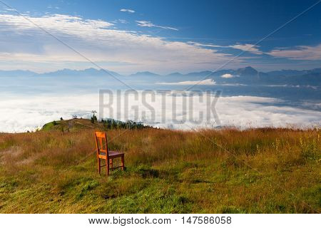 Old wooden chair on the top in Gerlitzen Apls in Austria.Inverse weather and view of the mountains in Slovenia.