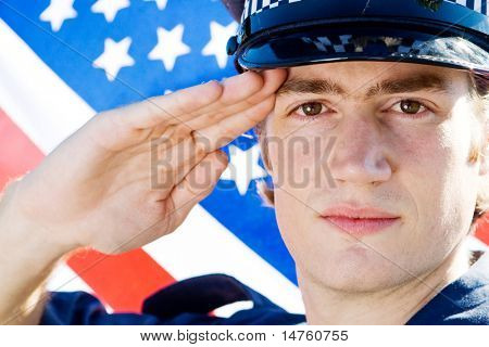 mladý americký policista zdravení, pozadí je vlajka USA