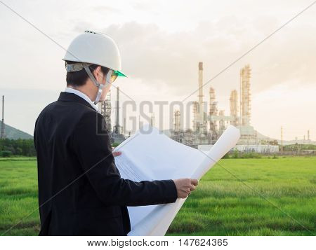 refinery engineer with white safety helmet see drawing standing in front of oil refinery building structure in heavy petrochemical refinery industry.