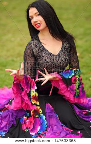 Young happy woman in beautiful skirt zingara poses on lawn outdoor