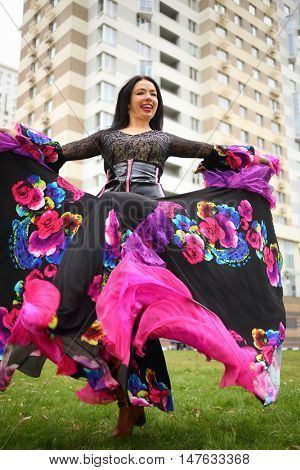 Young woman in beautiful skirt zingara dances on lawn near building
