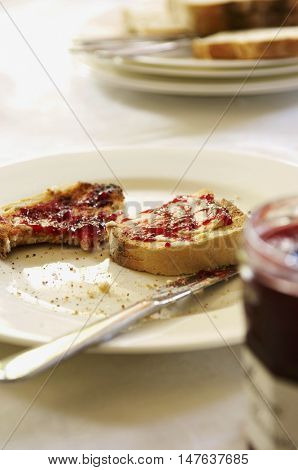 Closeup of a plate with half eaten toast covered in jam on table set for breakfast