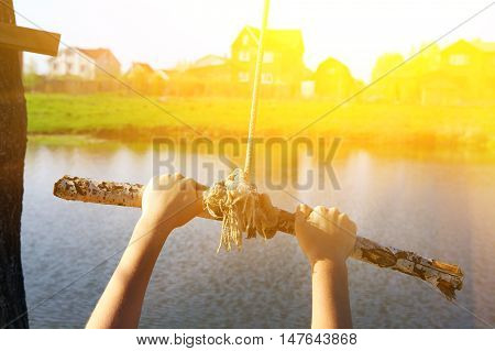 kids hands hold stick on swing rope close up photo on summer lake background ready to jump