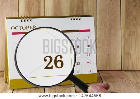 Magnifying glass in hand on calendar you can look Twenty-six date of monthFocus number Twenty-six in OctoberConcept in business and meetings.