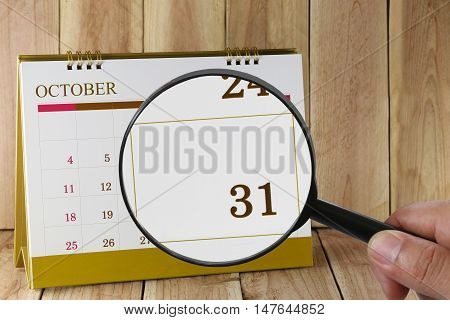 Magnifying glass in hand on calendar you can look thirty-one date of monthFocus number thirty one in OctoberConcept in business and meetings.