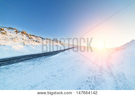 Icy winter road deicing sprinkled with black sand. Landscape with the rising sun.