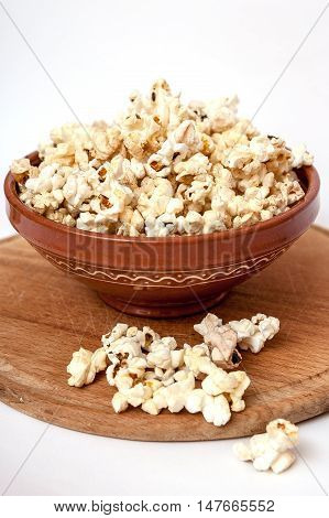 Wooden cutting board clay bowl full of popcorn some popcorn scattered.