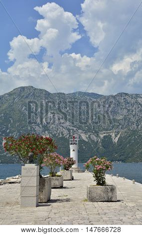 The artificially created island Our Lady of the Rock island in Kotor Bay Montenegro. Small oleander plants can be seen in the foreground and a small lighthouse in the background