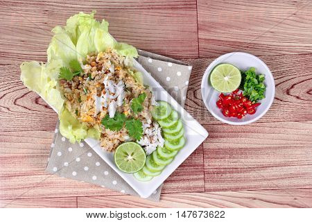 Fried rice with crab topped streamed crab,halve green lemon,sliced cucumber,lettuce and coriander  served  spicy  sour filling side dish  on wood.  Top view