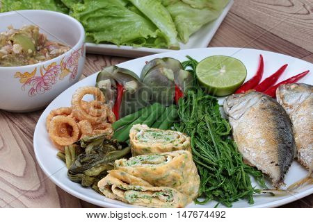 Close up of deep fired mackarel,vegetable omelet,pork rind,pickle lettuce,green lemon,red chili and boiled of eggplant,lentils,acacia and green chili dip as