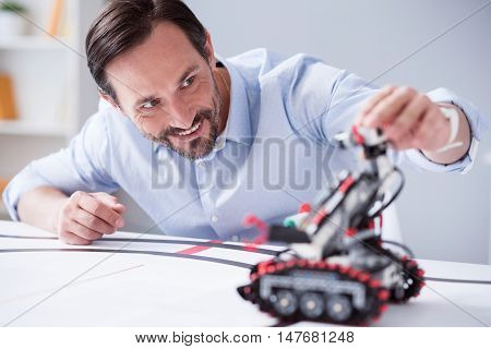 Happy creation. Green-eyed man with a beard testing the machine he has invented while leaning on the table