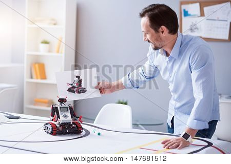Satisfied. Scientist looking at the picture of a robot and the real machine. Both items looking alike.