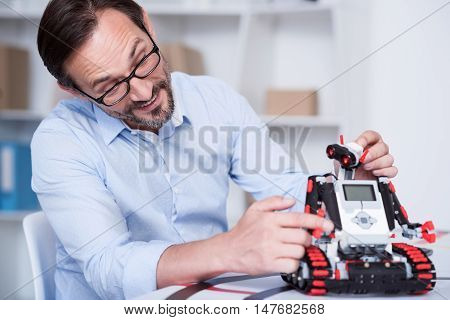 Fun time. Attractive Caucasian man tickling a robot as a pet