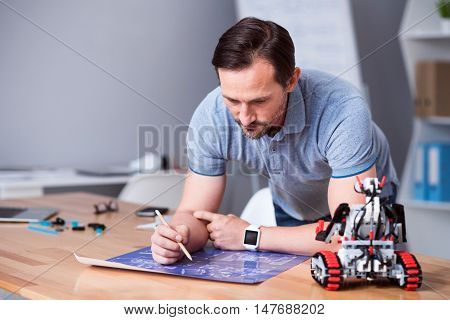 My project. Pleasant professional engineer working on the project and standing near table while testing robot