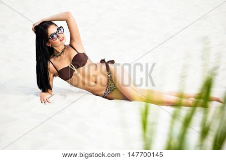 Fashion shoots girlfriend on the white sand in the swimsuit with glasses