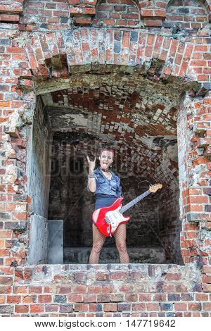 punk girl with red electric guitar standing in the window of hte abandoned castle