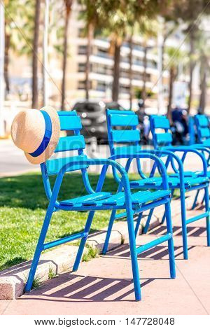 The blue chairs of the promenade with hat in Cannes city. This chairs are iconic symbol and tourist attraction of Cannes in France