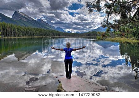 Woman by alpine lake with mountains and clouds reflection.  Honeymoon lake. Banff National Park. Canadian Rockies. Alberta. Canada.